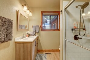 Un baño con tocador de madera, un espejo grande y una ducha con puerta de cristal.