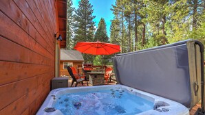 Ein Whirlpool mit einer Holzterrasse und einem Sonnenschirm, umgeben von Bäumen.