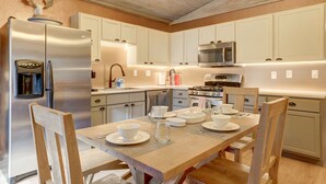 Eine moderne Küche mit weißen Schränken, Edelstahlgeräten und einem Esstisch aus Holz, gedeckt für vier Personen.