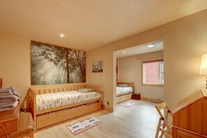 Un dormitorio con dos camas de madera, un cuadro grande de árboles, un escritorio pequeño y una silla.