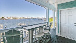 A covered porch with a view of a waterfront, featuring a table and chairs, and a white door. - FloraBama Inspired Waterfront Condo w/ Boat Slip next To The Famous Florabama  (Pensacola)
