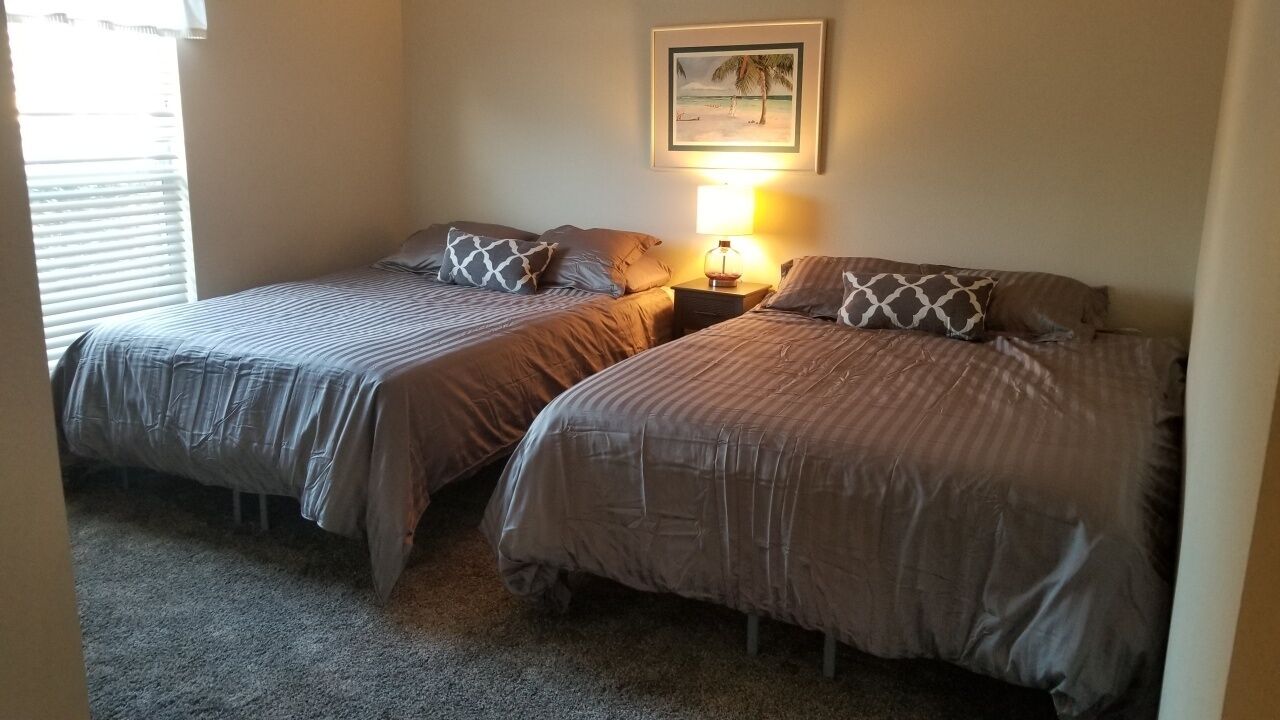 A bedroom with two single beds, a nightstand with a lamp, and a framed picture on the wall.