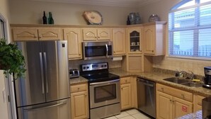 Una cocina con electrodomésticos de acero inoxidable, armarios de madera, encimera de granito y una ventana con persianas.