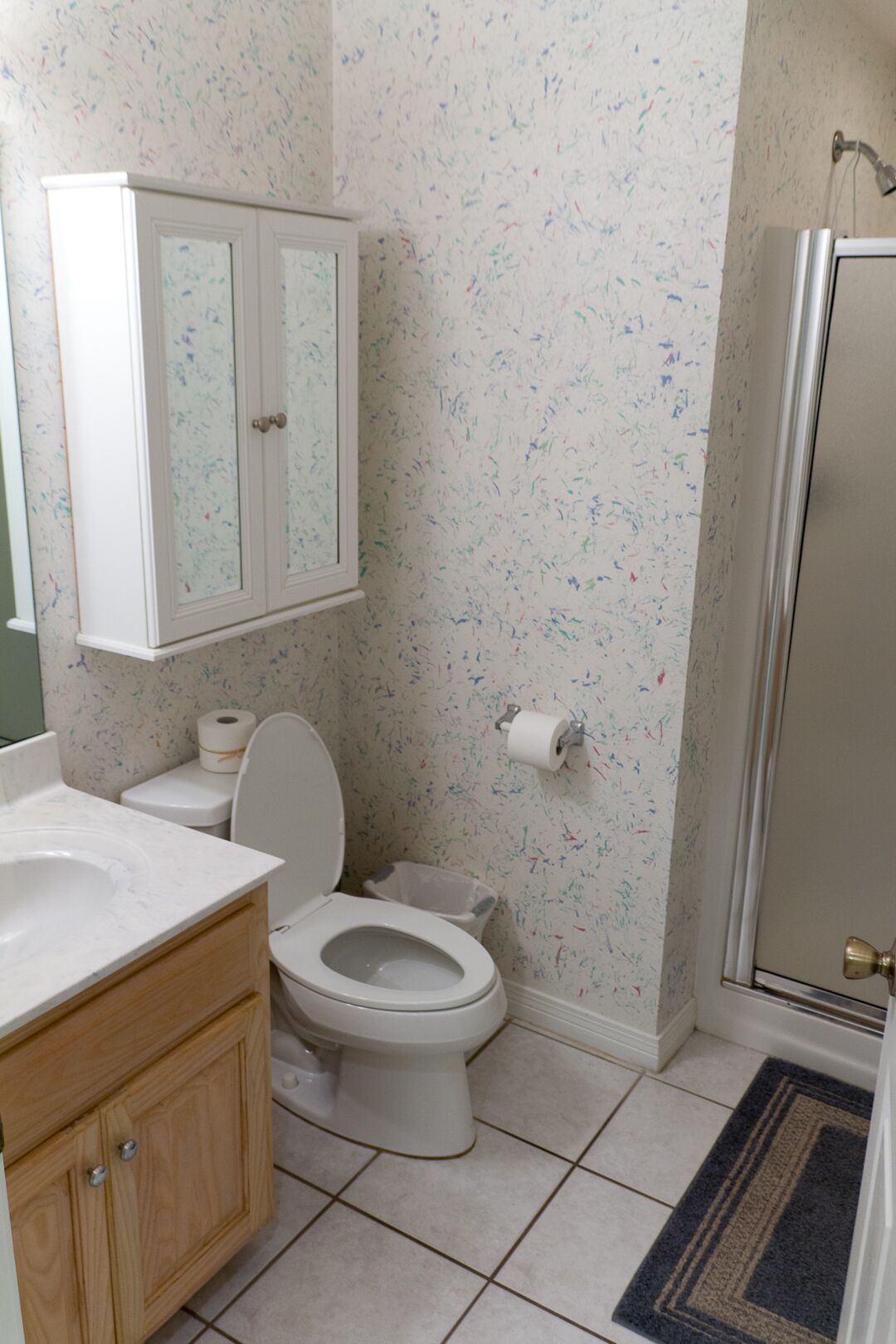 A bathroom with a toilet, a sink, a cabinet, and a shower area.