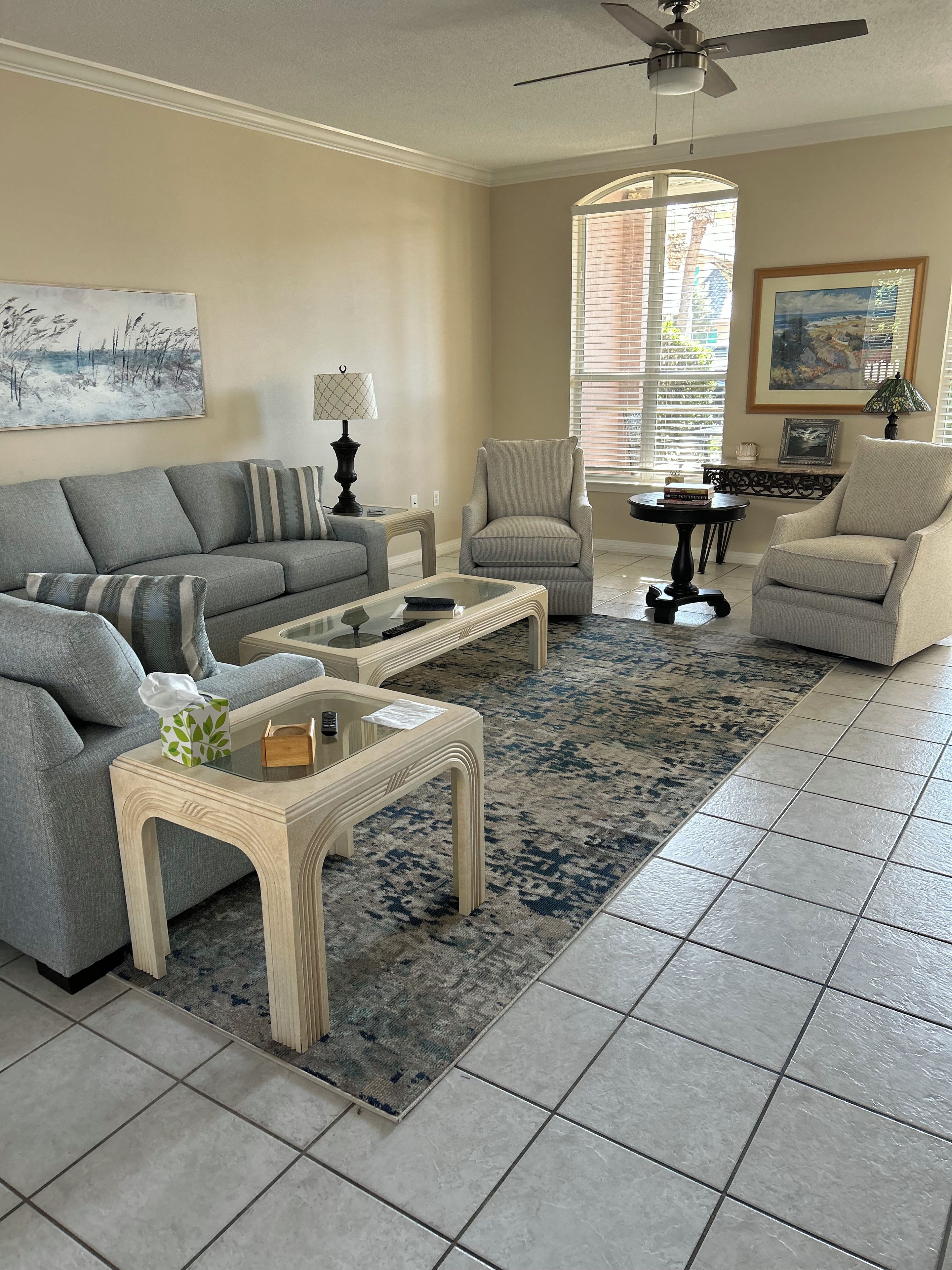 A living room with a sofa, armchairs, a coffee table, a rug, and a ceiling fan.