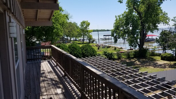 Une terrasse en bois avec une rambarde donnant sur un lac, entourée d’arbres et d’un quai.
