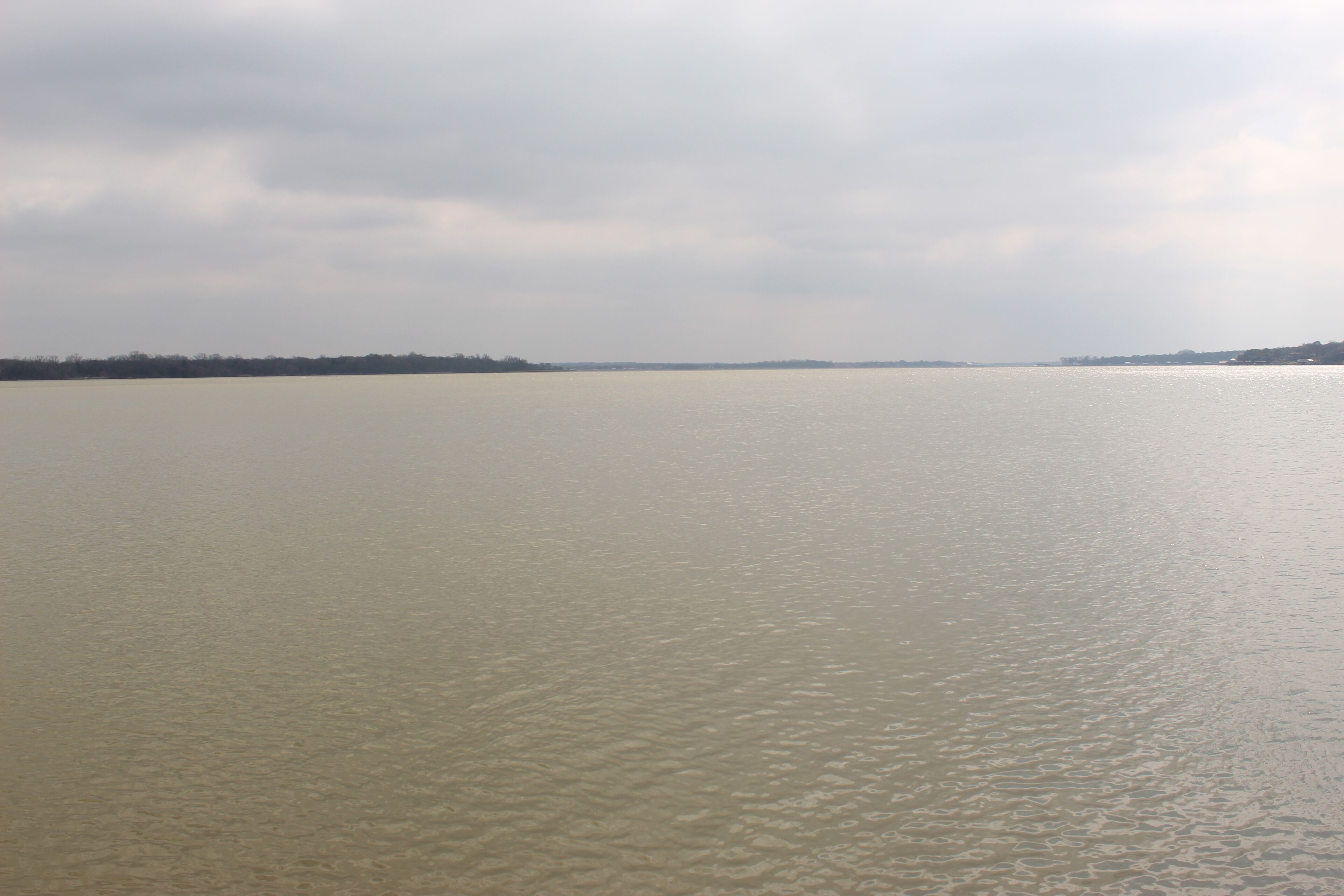 Une large rivière aux eaux calmes, avec une rive éloignée.