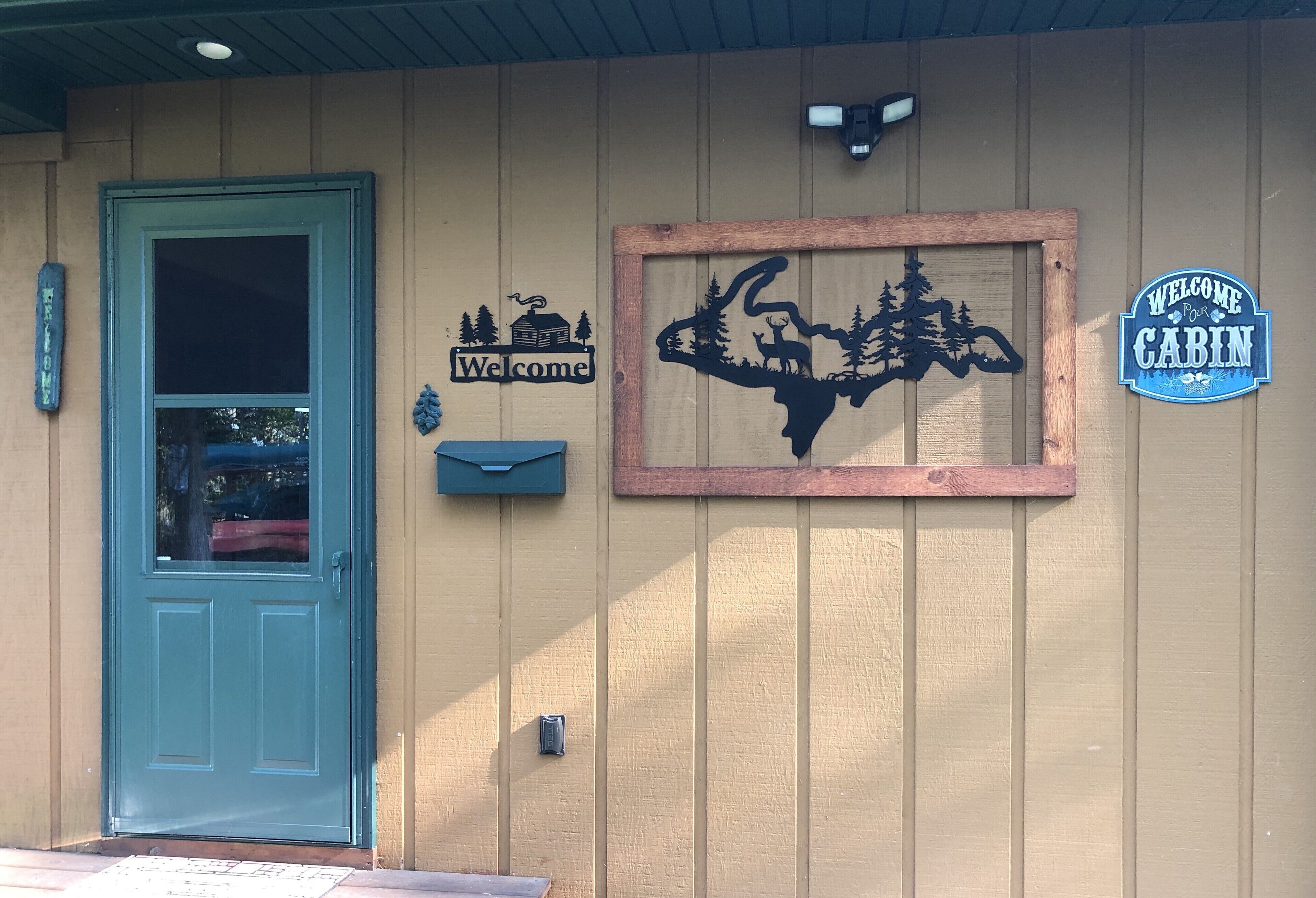 Eine Holzhütte mit blauer Tür, einem Willkommensschild, der Silhouette eines Baumes mit Tieren und einem Schild mit der Aufschrift 'Welcome to Cabin'.