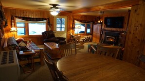 A cozy cabin interior with a wooden dining table, chairs, a sofa, a fireplace, and a television. - Quaint beautiful cabin on the southwest shore on AuTrain Lake (AuTrain)
