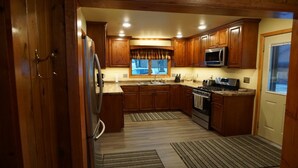 A kitchen with wooden cabinets, stainless steel appliances, and a window. - Quaint beautiful cabin on the southwest shore on AuTrain Lake (AuTrain)