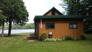 A small wooden cabin with a green roof, a front porch, and an American flag. - Quaint beautiful cabin on the southwest shore on AuTrain Lake (AuTrain)