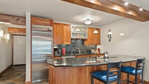 A modern kitchen with wooden cabinets, a stainless steel refrigerator, a granite countertop, and pendant lighting. - Lift One - Stylish remodeled one bedroom with view of Aspen Mountain (Aspen)