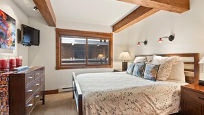 A bedroom with a bed, wooden headboard, a dresser, a TV, a window, and a lamp. - Lift One - Stylish remodeled one bedroom with view of Aspen Mountain (Aspen)