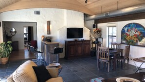 A spacious living area with a high ceiling, a TV, a coffee station, and a dining area with wooden furniture. - Rio de Arcadia - Two Riverside Homes, Pool & Hot Tub (Kerrville)