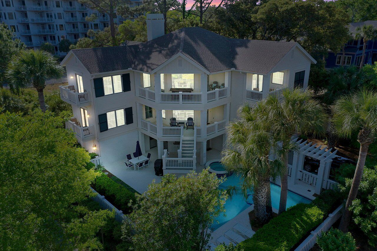 A multi-story house with a pool, surrounded by trees and a fence.