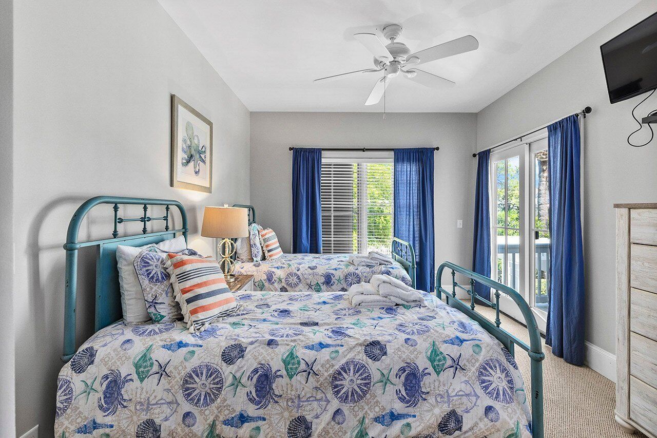 A bedroom with a bed, a ceiling fan, a window with curtains, and a TV mounted on the wall.
