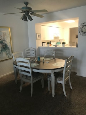 Un coin repas avec une table ronde, des chaises blanches et un ventilateur de plafond.