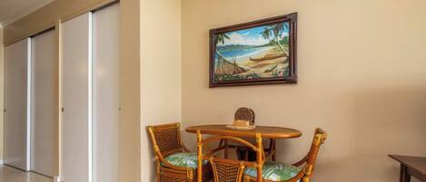 A room with a dining table and chairs, a painting of a beach scene, and a closed door.