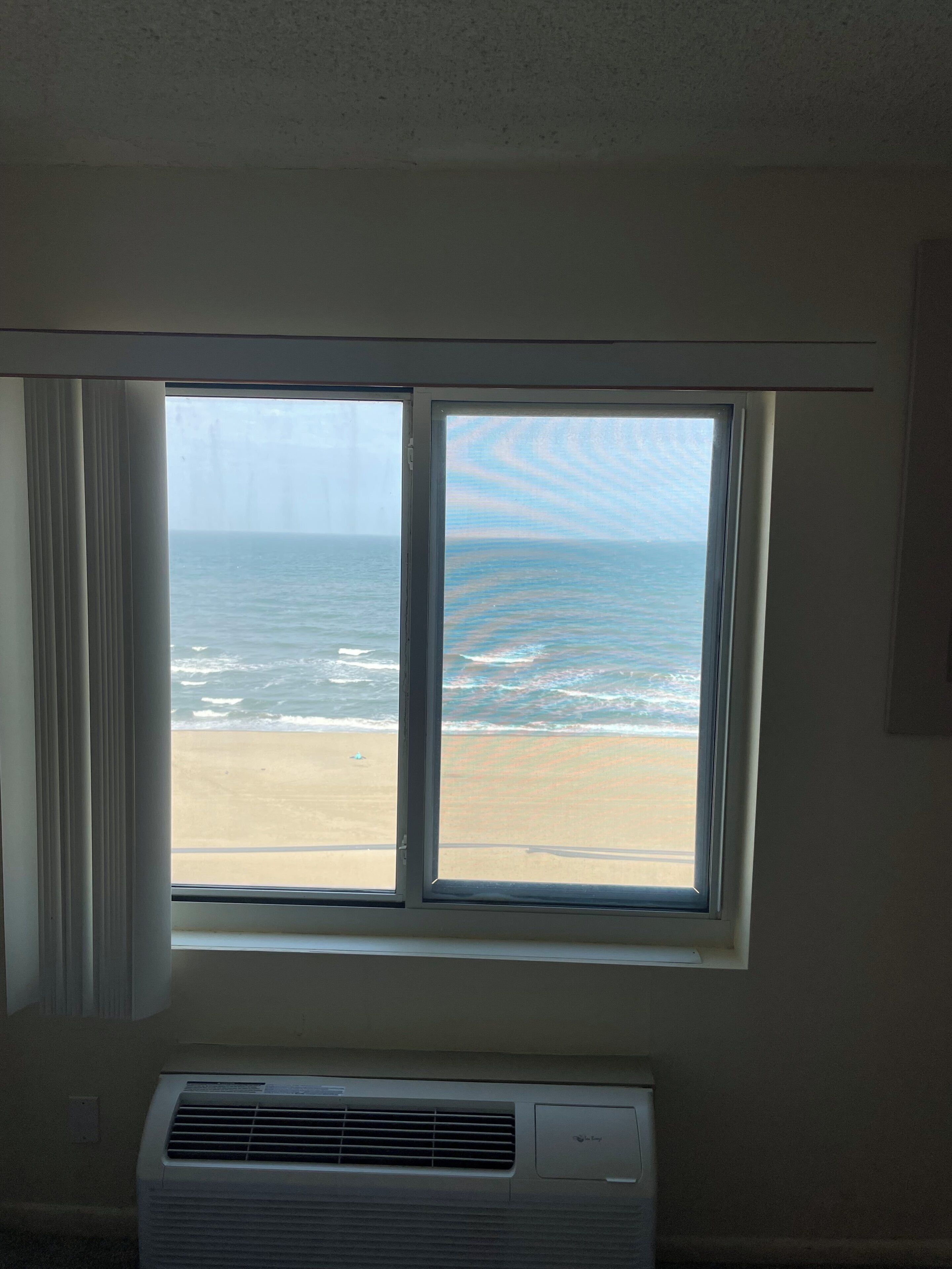 A room with a large window overlooking a beach, a wall-mounted air conditioner, and a plain wall.