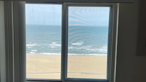 Habitació amb una finestra gran que dona a una platja, aire condicionat fixat a la paret i una paret senzilla.