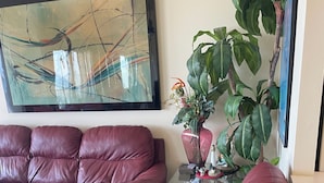 Un saló amb un quadre abstracte gran, un sofà de pell marró, una taula de centre de vidre i una planta en test.