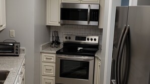 A modern kitchen with white cabinets, stainless steel appliances, and a herringbone-patterned floor.