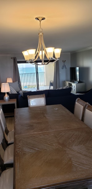 Enjoy ocean views from the large window in this stylish room, featuring a dining area with a table and chairs, a chandelier, and a TV.