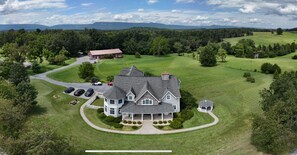 Une grande maison dotée d’une véranda qui fait le tour de la maison, d’un garage et d’une allée où sont garées des voitures.