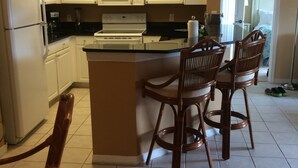 A kitchen with white cabinets, a central island with bar stools, a microwave, and a refrigerator.