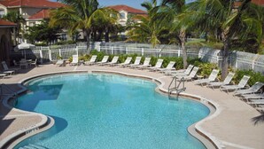 A large, curved swimming pool with a white fence surrounding it, and several lounge chairs along the edge.
