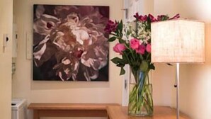 Een kamer met een houten bureau, een lamp, een bloemenvaas en een schilderij aan de muur.