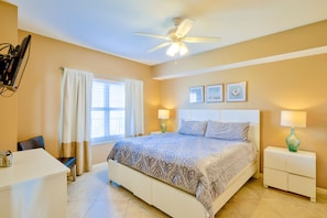 A bedroom with a bed, bedside lamps, a ceiling fan, a desk, and a chair.