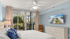 A bedroom with a bed, a ceiling fan, a TV, and a view of a resort. - Waterscape C200 ~ Ground Floor 3BR ~ Easy Access to Waterpark (Fort Walton Beach)