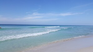 Een strand met helder turquoise water, zachte golven en een zandstrand.