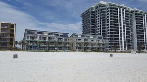 Hotel aan het strand met meerdere balkons, een zandstrand voorop en een heldere lucht.
