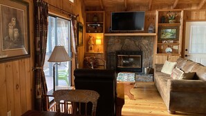 L’intérieur chaleureux d’un chalet avec un plafond en bois, une cheminée, un téléviseur et un canapé.