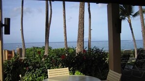 A covered outdoor seating area with a table and chairs, overlooking the ocean with palm trees. - Wailea Ekahi 14F - Best Views -  3 Minutes Walk to Beach (Wailea-Makena)