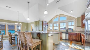 Una cocina amplia con una isla grande, taburetes de bar de madera y vistas al exterior a través de ventanales.