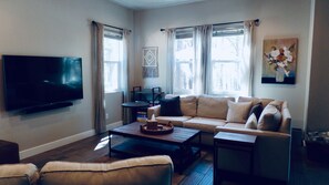 Una sala de estar con televisor de pantalla plana, un sofá, una mesa de centro y una mesita auxiliar.