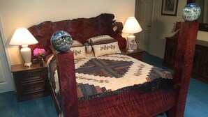 Un dormitorio con una cama de madera, dos mesitas de noche con lámparas, un globo decorativo y un edredón estampado con motivos florales.