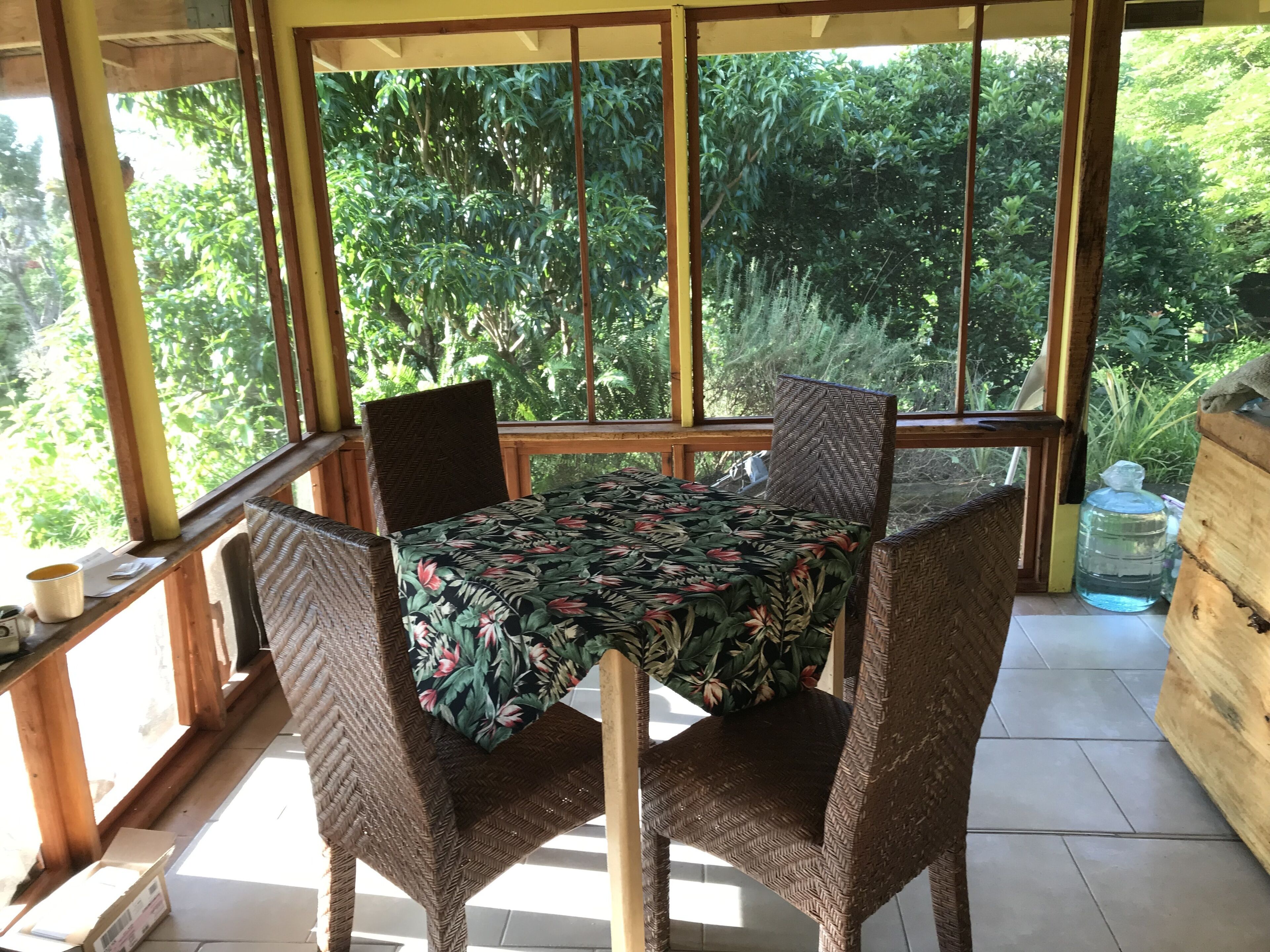 A room with a table and chairs, large windows, and a view of greenery outside.