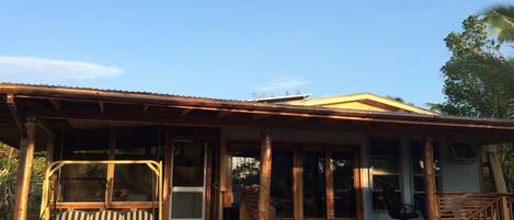 A wooden house with a porch, large windows, and a screened door.