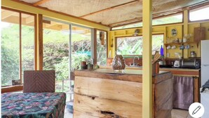 Cocina rústica con mostrador de madera, un lavamanos y un refrigerador. Hay una ventana que ofrece vistas de la vegetación.
