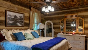 A log cabin bedroom with a bed, dresser, mirror, and ceiling fan. - Vintage 1850's log house for rent with 185 acres  ,on a Creek ,  2miles trails . (Vanleer)