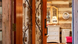 A wooden door with a decorative metal vine design, a white wicker dresser, and a red towel on a chair. - Vintage 1850's log house for rent with 185 acres  ,on a Creek ,  2miles trails . (Vanleer)