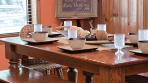 Una mesa de madera para comer con varios cuencos y vasos, una pizarra con escritura, y una ventana al fondo.