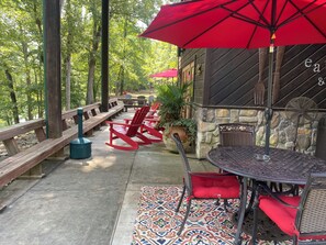 Un espace extérieur abrité avec des bancs en bois et des fauteuils à bascule rouges, un mur en pierre avec un barbecue et un parasol rouge.