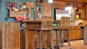 Una cocina rústica con taburetes de madera, un refrigerador y un letrero de bar.