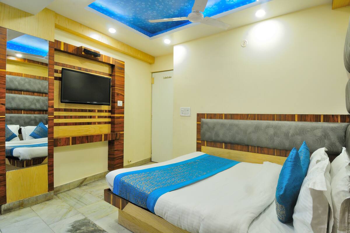 Une chambre d’hôtel dotée d’un grand lit, d’un téléviseur à écran plat fixé au mur et d’un plafond orné d’un motif lumineux bleu.