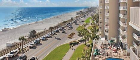 A hotel with a pool, a beach view, and a parking lot with cars.